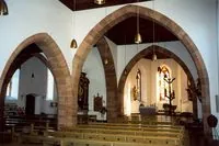 Innenraum mit Sandsteinbögen, Kirchenbänken und Blick zum Altar.