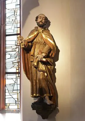 Goldene Statue des Heiligen Petrus mit Schlüsseln neben Glasfenster.