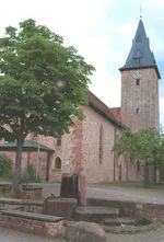Außenansicht St. Johannes Nepomuk mit Kirchturm und Brunnen.