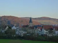 Ortsansicht Biebergemünd mit Kirchturm vor herbstlichen Hügeln.