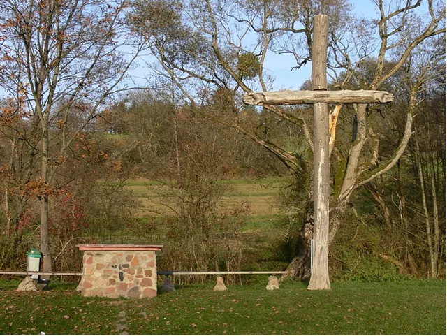 Steinerner Außenaltar und großes rustikales Holzkreuz im Grünen.