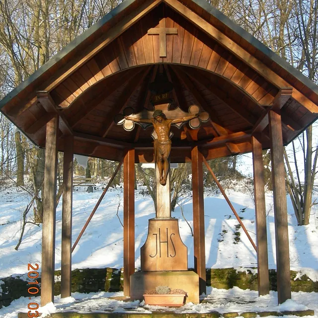 Hölzerne Kreuzigungsgruppe im Freien mit JHS-Inschrift im Schnee.